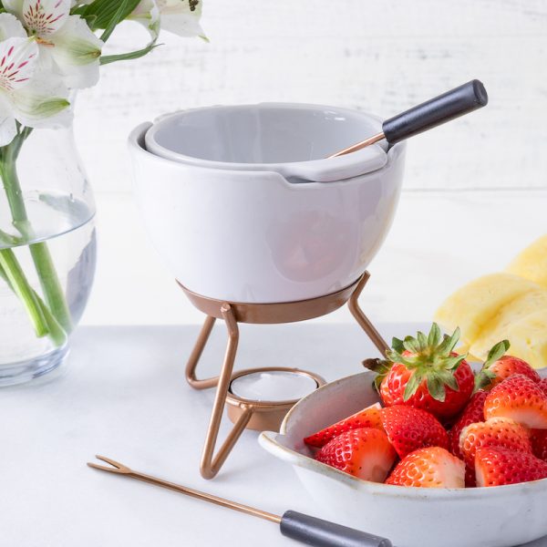 white fondue set sitting next to bowl of fresh fruit